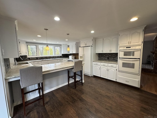 kitchen with white appliances, a kitchen breakfast bar, dark wood-style flooring, a peninsula, and a sink