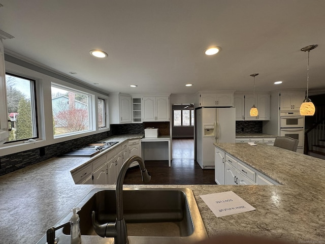 kitchen with white appliances, backsplash, a sink, and white cabinets