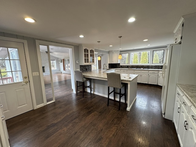 kitchen featuring dark wood-style flooring, a breakfast bar area, freestanding refrigerator, white cabinets, and a sink