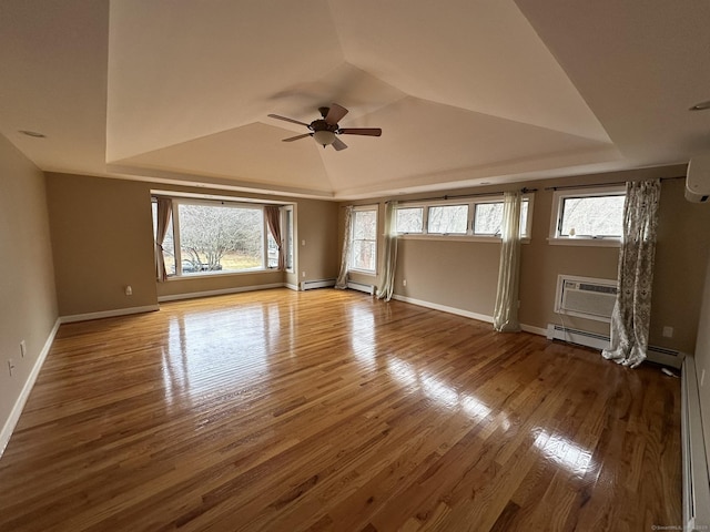 empty room with a wealth of natural light, a wall mounted AC, a raised ceiling, and hardwood / wood-style flooring