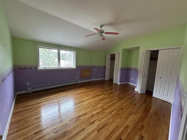 unfurnished bedroom with a baseboard radiator, vaulted ceiling, two closets, and wood finished floors