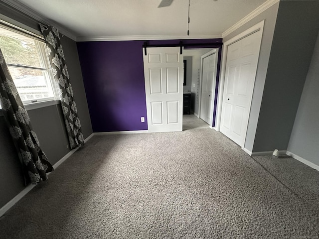 unfurnished bedroom featuring carpet, a barn door, baseboards, and crown molding