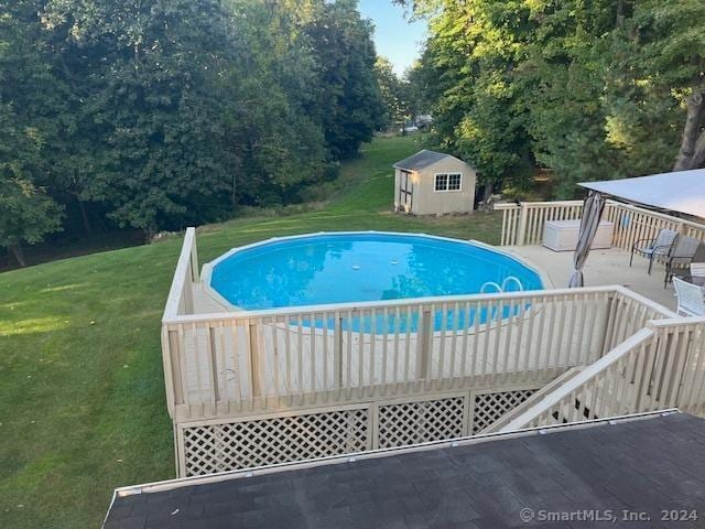 view of pool with a wooden deck, a storage unit, and a lawn