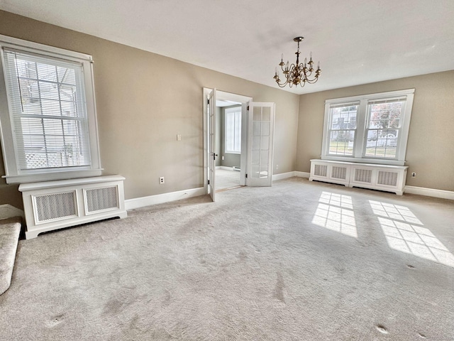 unfurnished room featuring light carpet, a notable chandelier, radiator heating unit, and plenty of natural light