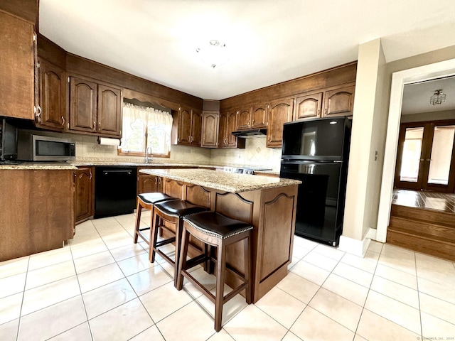 kitchen with decorative backsplash, light tile patterned floors, a kitchen island, a breakfast bar, and black appliances