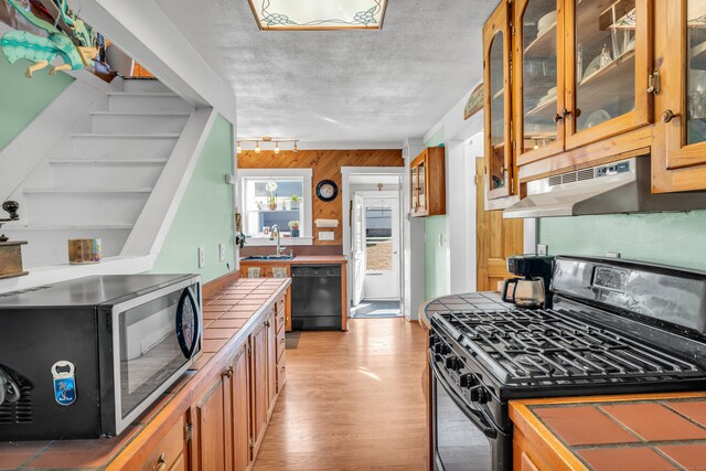 kitchen with tile countertops, a textured ceiling, black appliances, light hardwood / wood-style floors, and sink