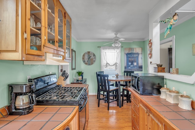 kitchen featuring black appliances, light wood-type flooring, ceiling fan, tile counters, and crown molding