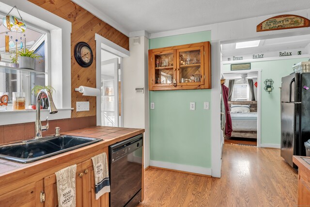 kitchen featuring wood walls, black appliances, sink, tile countertops, and light hardwood / wood-style flooring