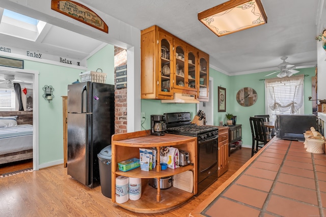 kitchen with tile counters, light hardwood / wood-style flooring, crown molding, black appliances, and ceiling fan