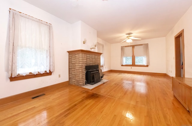 unfurnished living room with light hardwood / wood-style flooring, a wood stove, and ceiling fan