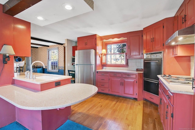 kitchen featuring sink, light wood-type flooring, electric stovetop, a breakfast bar area, and stainless steel refrigerator