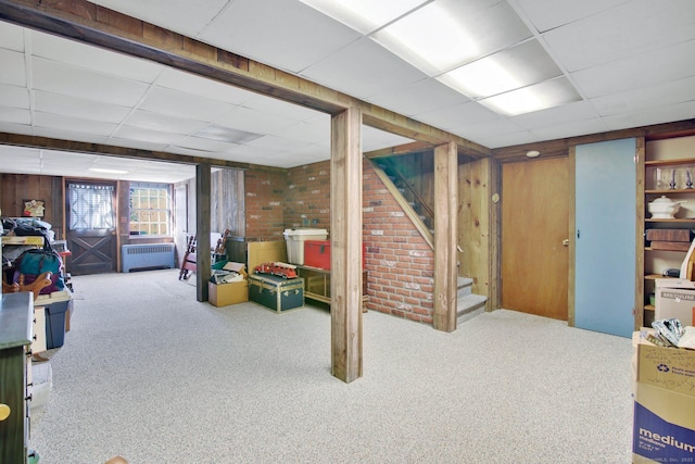 basement with brick wall, carpet flooring, a paneled ceiling, and wooden walls