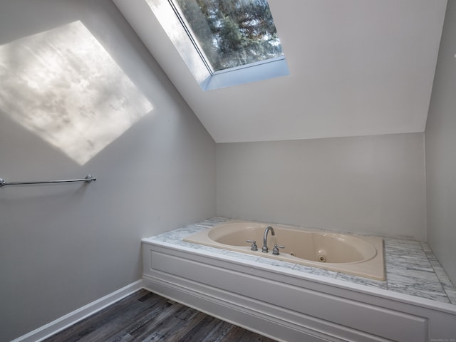 bathroom with vaulted ceiling with skylight, a tub, and hardwood / wood-style flooring