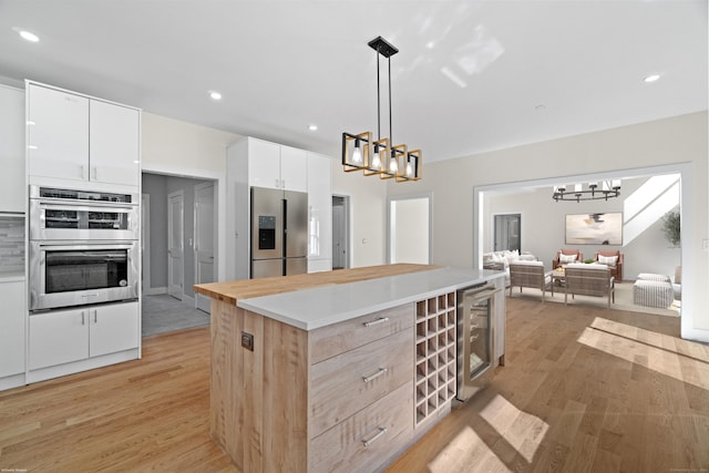 kitchen with white cabinets, stainless steel appliances, beverage cooler, and decorative light fixtures