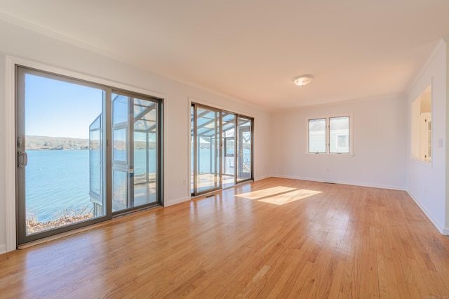 spare room with ornamental molding, a water view, and light wood-type flooring