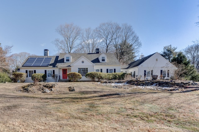 view of front of property with a front yard, roof mounted solar panels, and a chimney