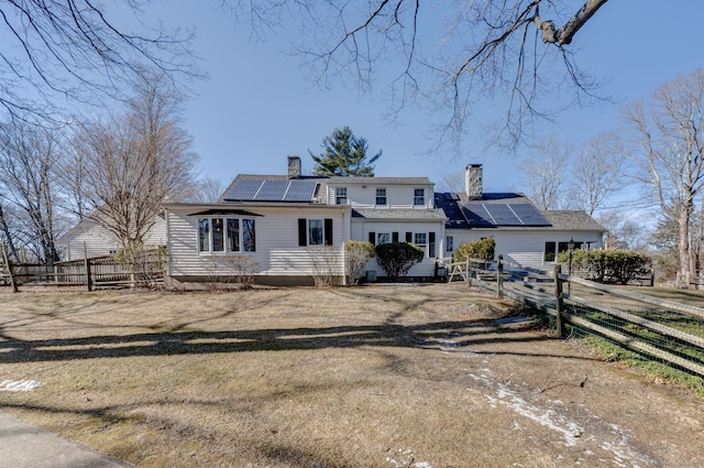 view of front facade with fence, a chimney, dirt driveway, and solar panels