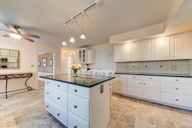 kitchen with stainless steel microwave, backsplash, white cabinets, a kitchen island, and dark stone counters