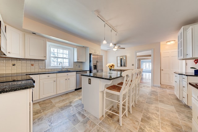 kitchen featuring stainless steel appliances, a sink, a kitchen breakfast bar, backsplash, and a center island