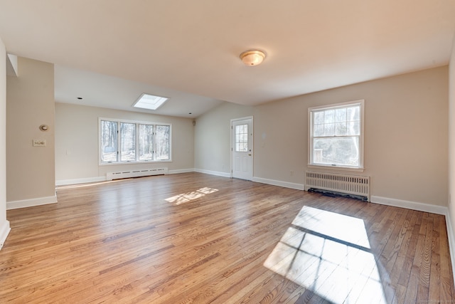 empty room featuring a skylight, baseboard heating, radiator heating unit, light wood-style floors, and baseboards