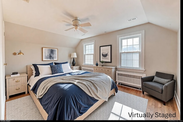 bedroom featuring lofted ceiling, radiator, visible vents, and wood finished floors