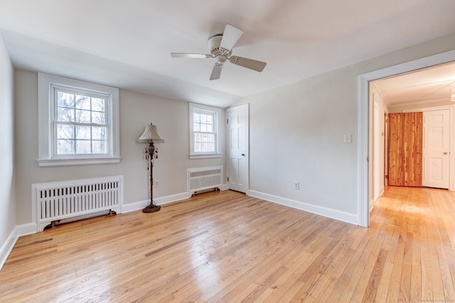 empty room with a ceiling fan, radiator, baseboards, and light wood finished floors