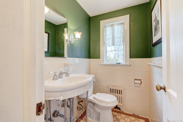 half bath with toilet, radiator, tile walls, and wainscoting