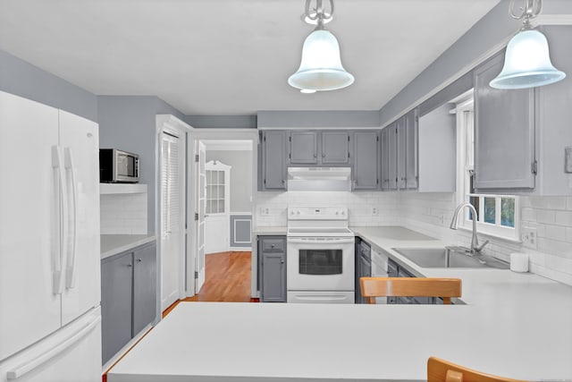 kitchen featuring tasteful backsplash, light wood-type flooring, pendant lighting, sink, and white appliances