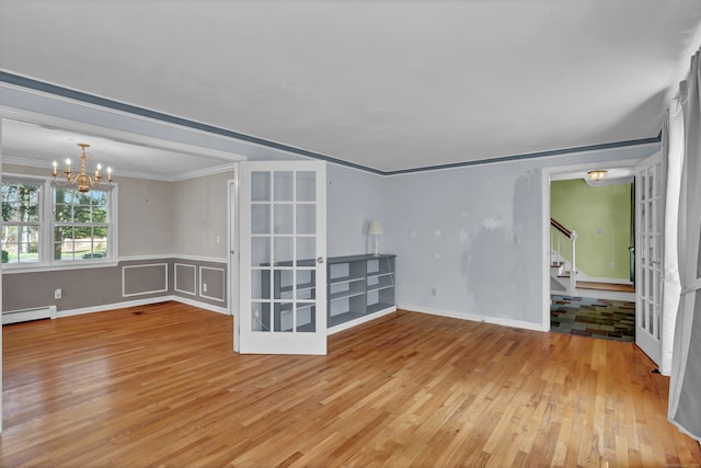 spare room featuring french doors, ornamental molding, a notable chandelier, a baseboard radiator, and light hardwood / wood-style floors