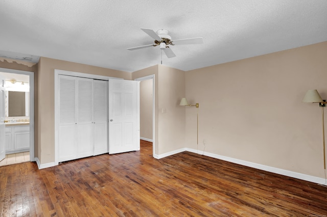 unfurnished bedroom featuring a textured ceiling, a closet, ceiling fan, connected bathroom, and dark hardwood / wood-style floors