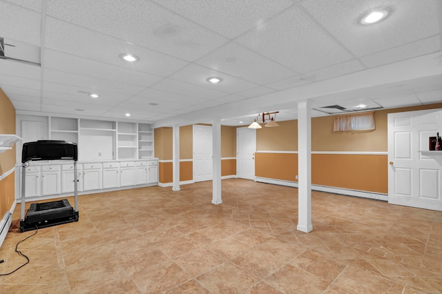 basement with a baseboard radiator, a drop ceiling, built in features, and light tile patterned floors