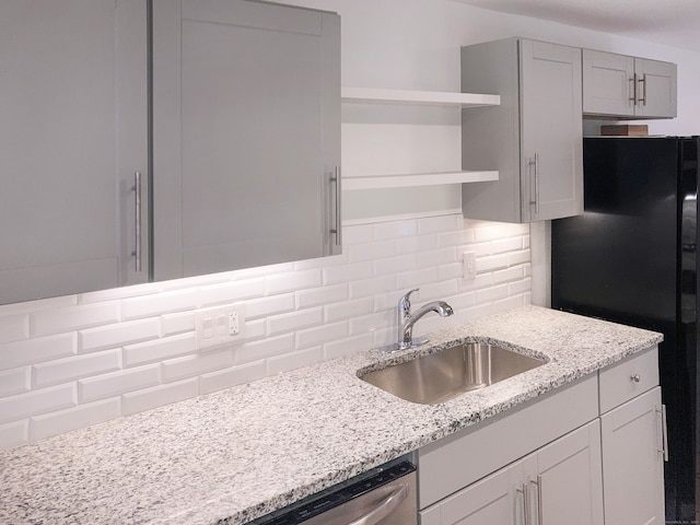 kitchen featuring light stone counters, sink, backsplash, and black refrigerator