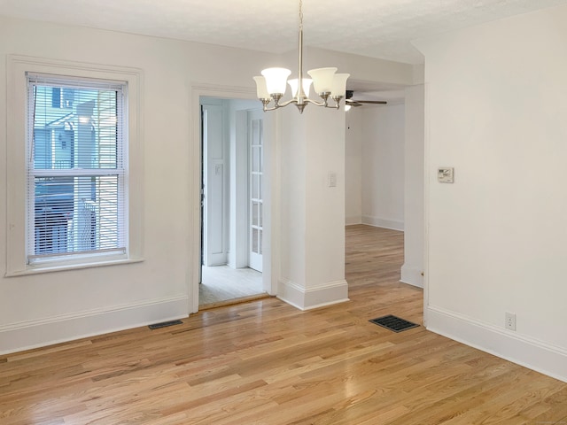 unfurnished dining area with a textured ceiling, ceiling fan with notable chandelier, and light hardwood / wood-style floors