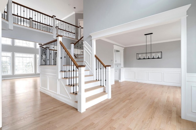 stairway with a decorative wall, ornamental molding, a high ceiling, and wood finished floors