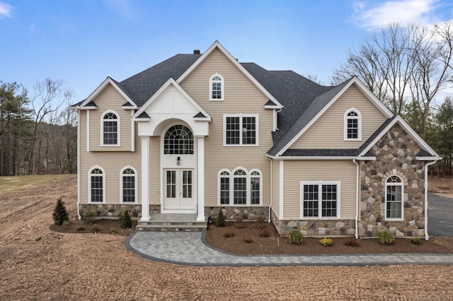 traditional home featuring french doors, stone siding, a chimney, and a shingled roof