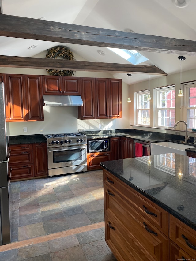 kitchen featuring appliances with stainless steel finishes, vaulted ceiling with skylight, sink, decorative light fixtures, and dark stone countertops