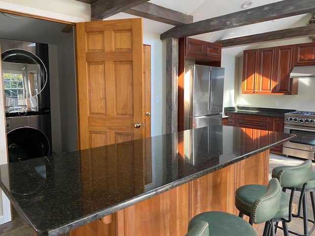 kitchen with stainless steel appliances, beamed ceiling, stacked washer and dryer, dark stone counters, and exhaust hood