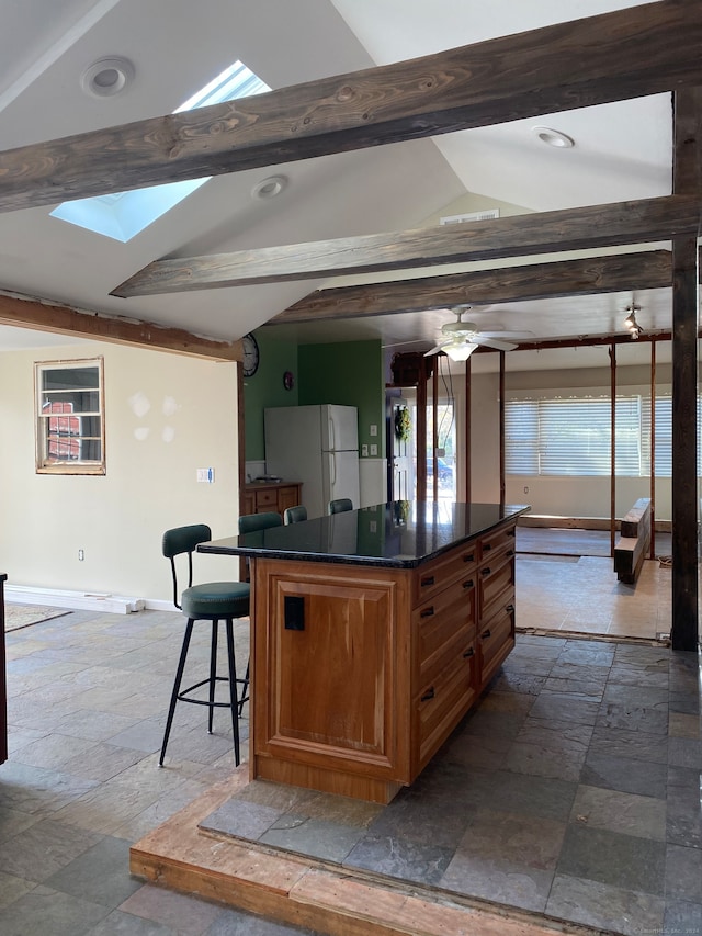 kitchen featuring a kitchen breakfast bar, lofted ceiling with skylight, ceiling fan, white fridge, and a kitchen island