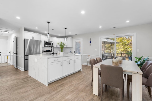 kitchen featuring light wood-type flooring, an island with sink, white cabinetry, stainless steel appliances, and pendant lighting