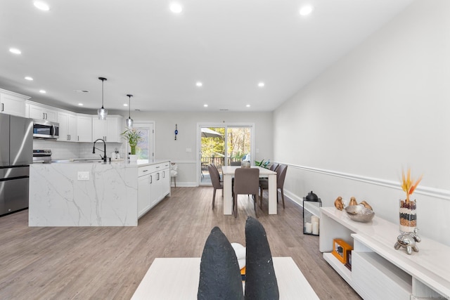 kitchen featuring white cabinets, hanging light fixtures, light stone countertops, light hardwood / wood-style flooring, and stainless steel appliances