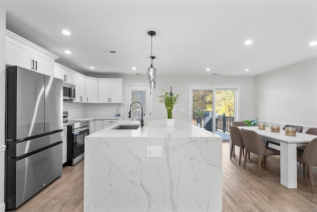 kitchen with sink, stainless steel appliances, white cabinets, light hardwood / wood-style flooring, and a center island with sink