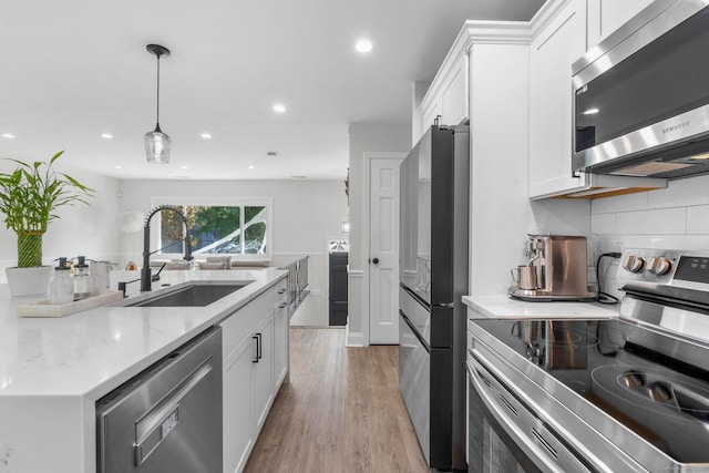 kitchen featuring sink, light wood-type flooring, hanging light fixtures, stainless steel appliances, and white cabinets