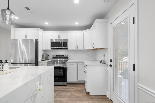 kitchen with appliances with stainless steel finishes, light stone counters, pendant lighting, and white cabinetry