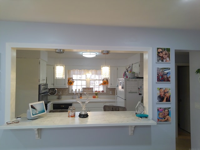 kitchen featuring kitchen peninsula, white cabinets, backsplash, pendant lighting, and white refrigerator