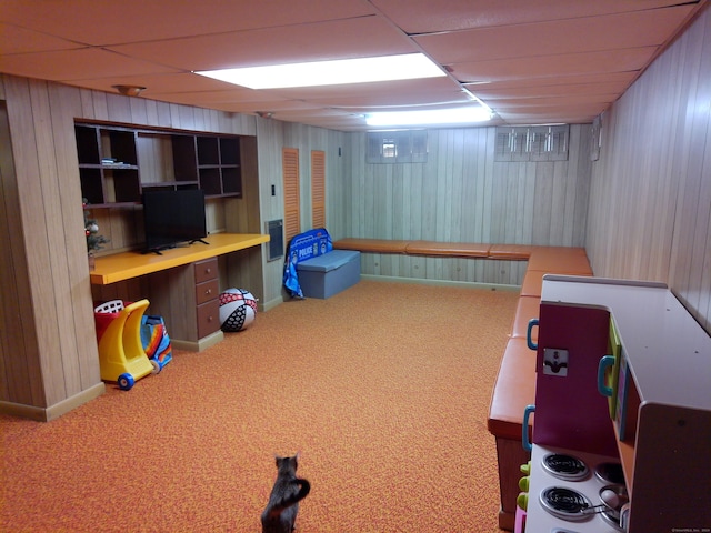 basement featuring a paneled ceiling, carpet floors, and wooden walls