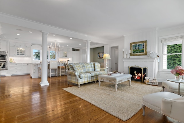 living room featuring dark wood-type flooring, ornamental molding, a brick fireplace, and ornate columns