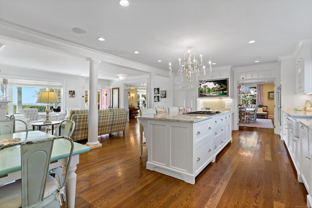 kitchen with light stone counters, a kitchen island, white cabinets, and ornate columns