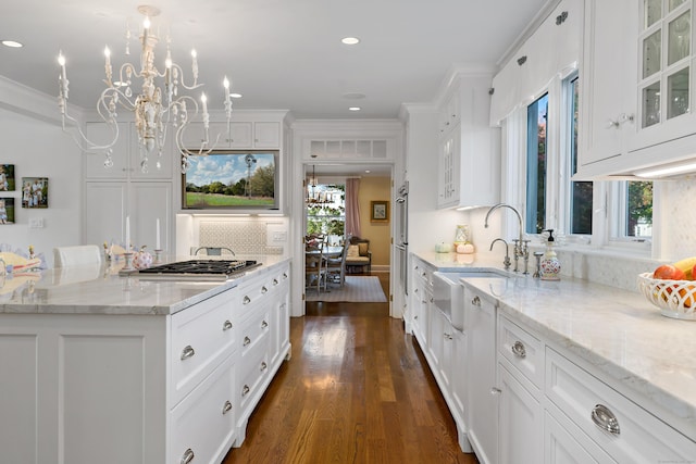 kitchen featuring hanging light fixtures, light stone countertops, sink, and white cabinets