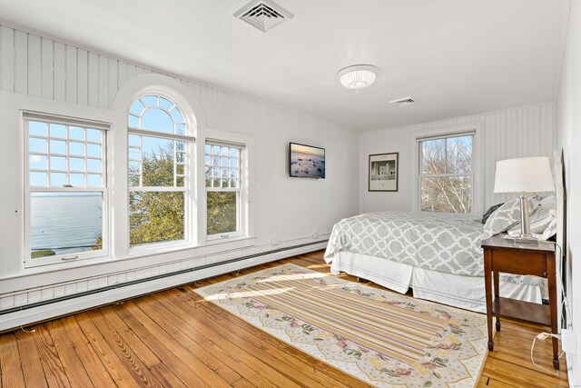 bedroom with multiple windows, light hardwood / wood-style floors, and baseboard heating