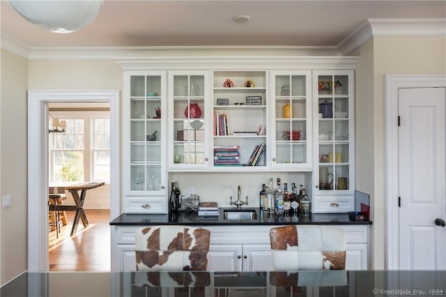 bar featuring white cabinetry, ornamental molding, light hardwood / wood-style flooring, and sink